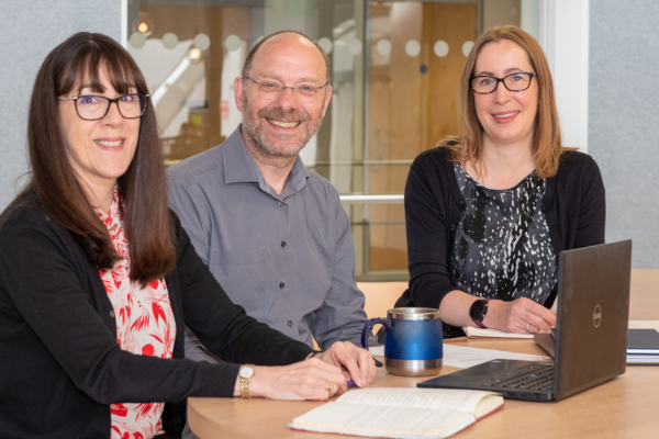 3 people at desk smiling