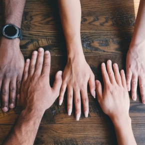 Five hands, side-by-side, on a wooded table