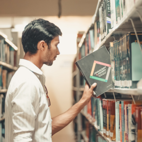 A young man pulling a book from a bookshelf