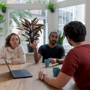 Three people sitting at a table, around a laptop